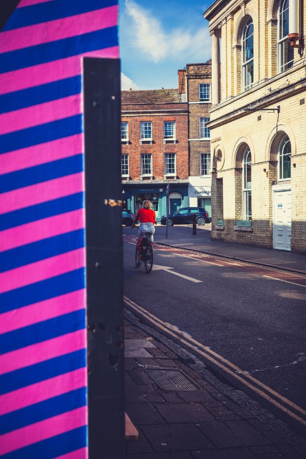  Street photo of woman on bike cycling away, with wall prominent in foreground<