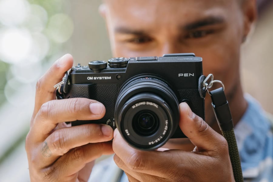  Photo of man holding OM SYSTEM PEN mirrorless camera<